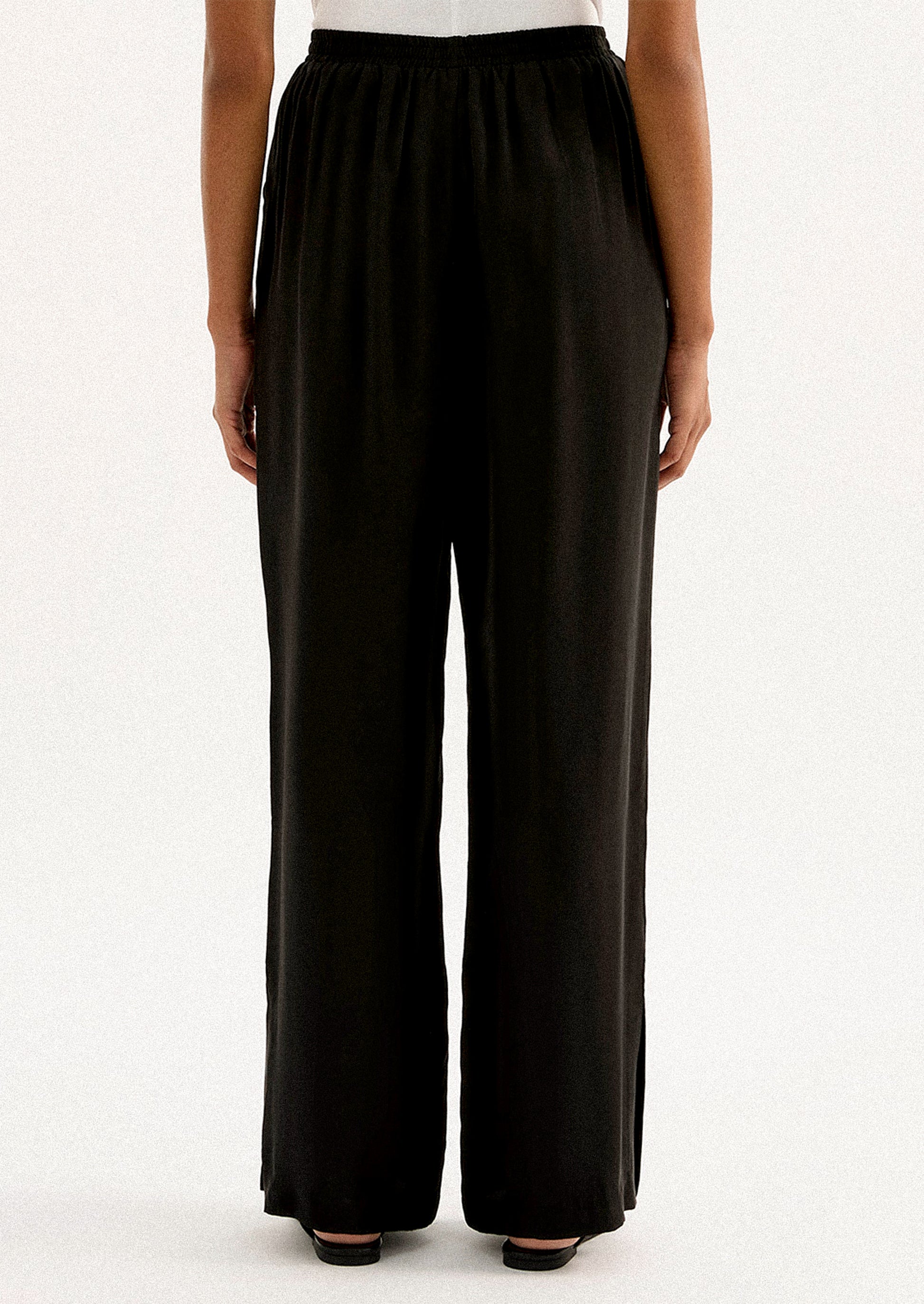 A person wearing a pair of black sateen pants with split leg hem.