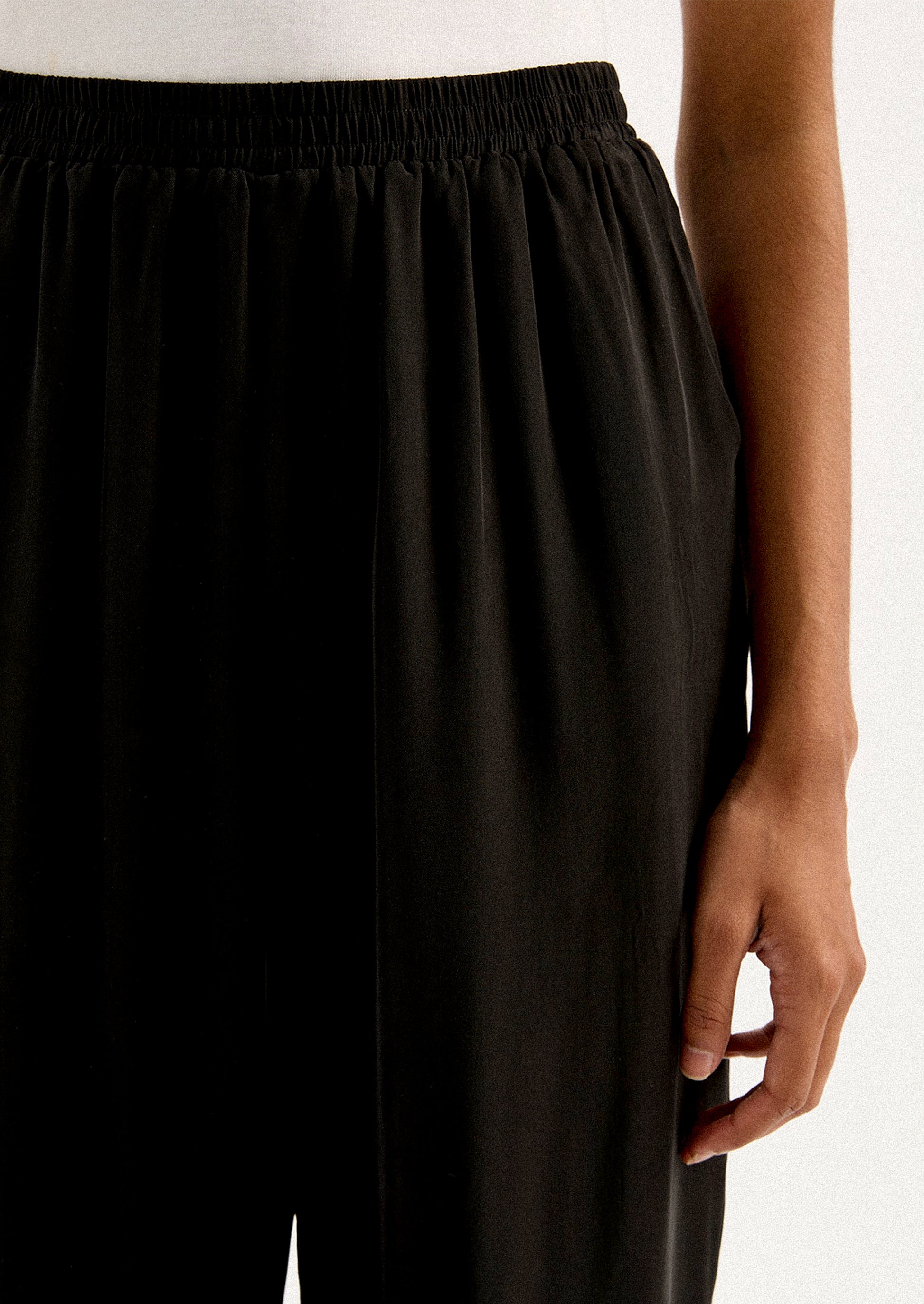 A person wearing a pair of black sateen pants with split leg hem.