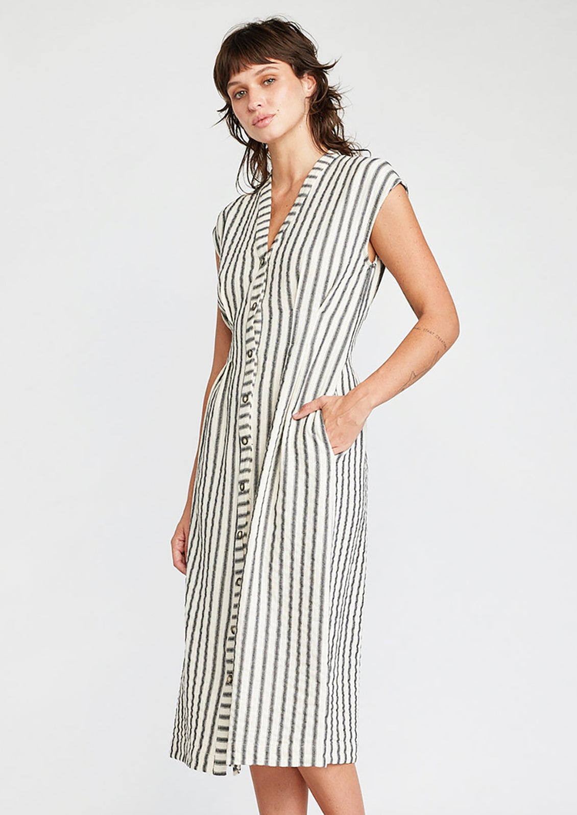 A woman wearing a sleeveless v-neck dress in white with black vertical stripes.