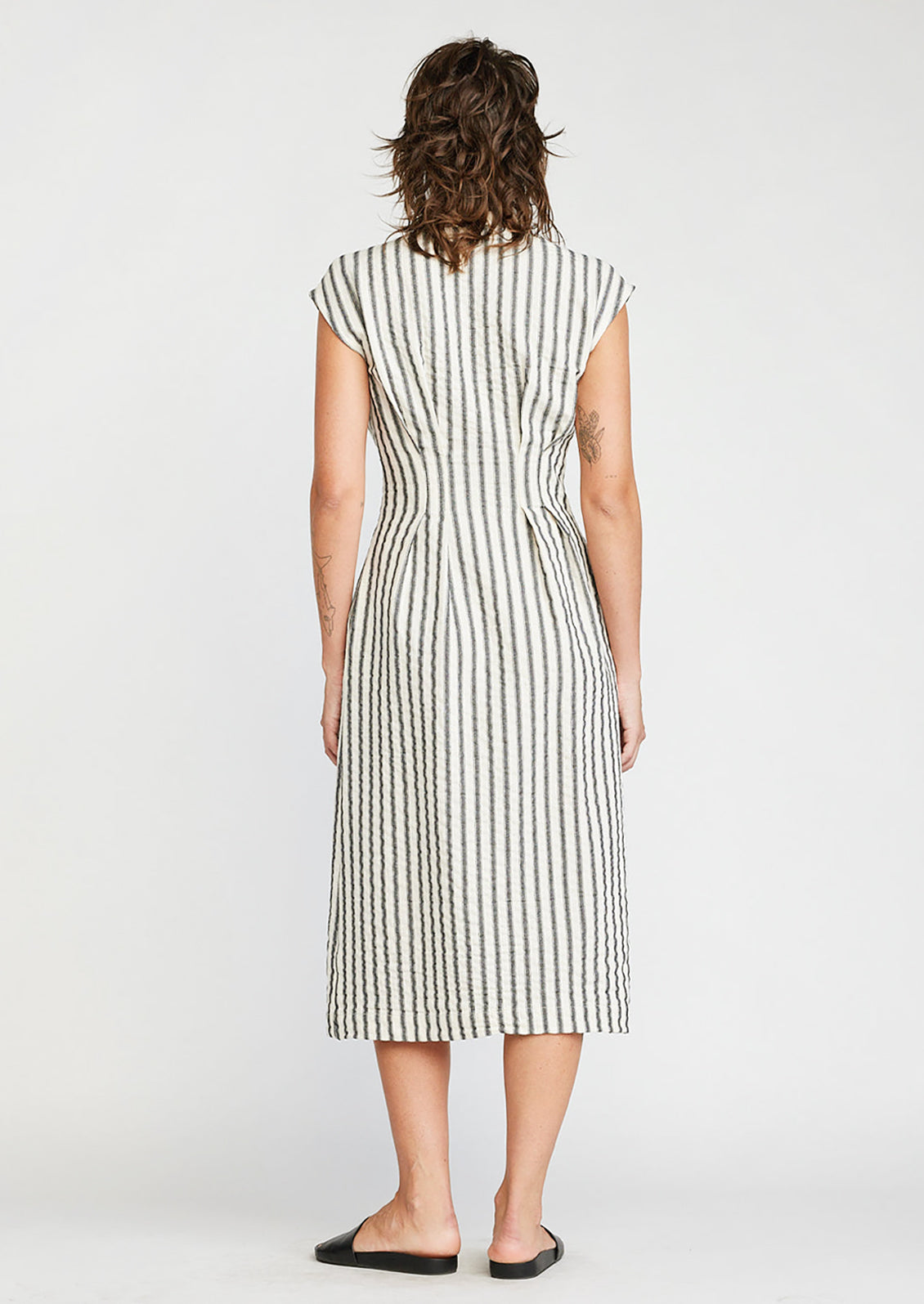 A woman wearing a sleeveless v-neck dress in white with black vertical stripes.