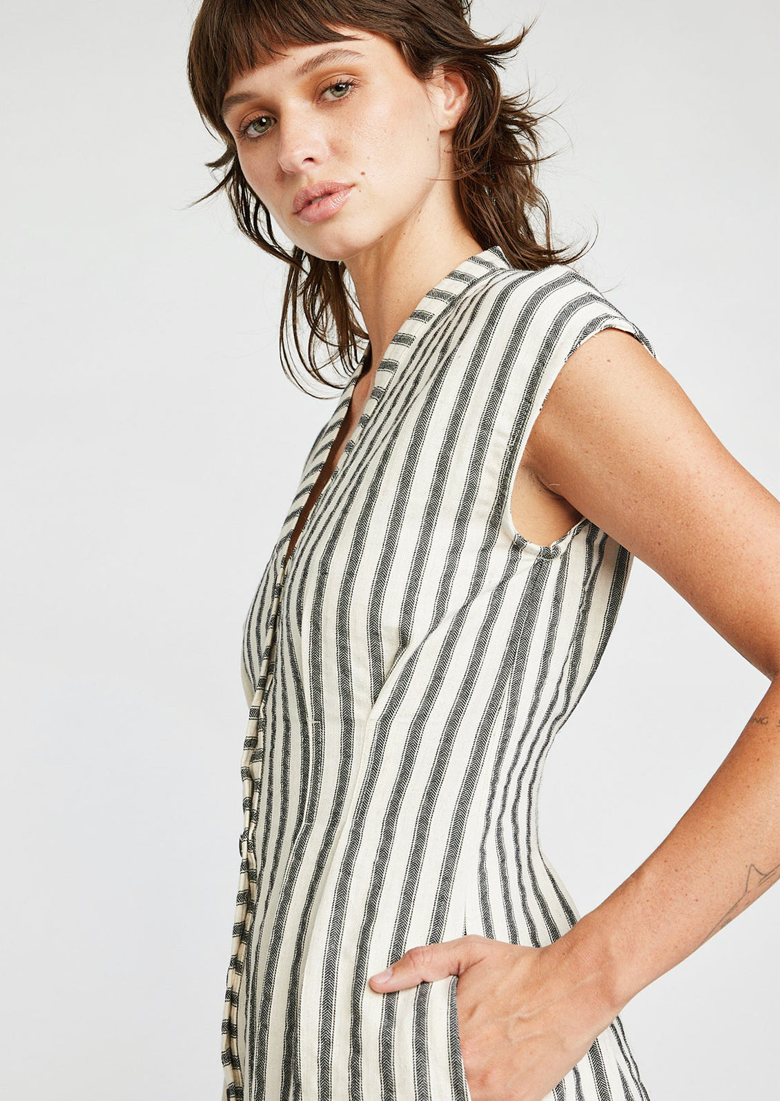 A woman wearing a sleeveless v-neck dress in white with black vertical stripes.
