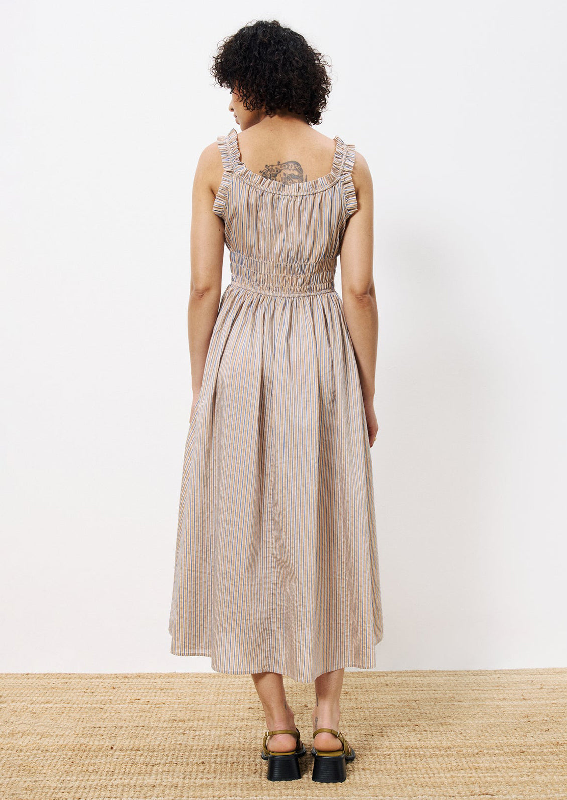 A woman wearing a smocked waist dress with ruffle trim, in brown and blue pinstripe.