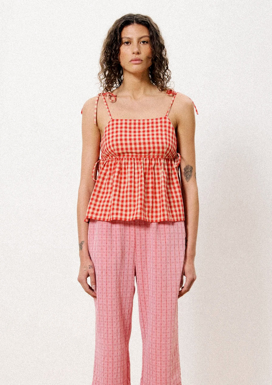 A woman wearing a tank top with shoulder ties in red and beige gingham fabric.