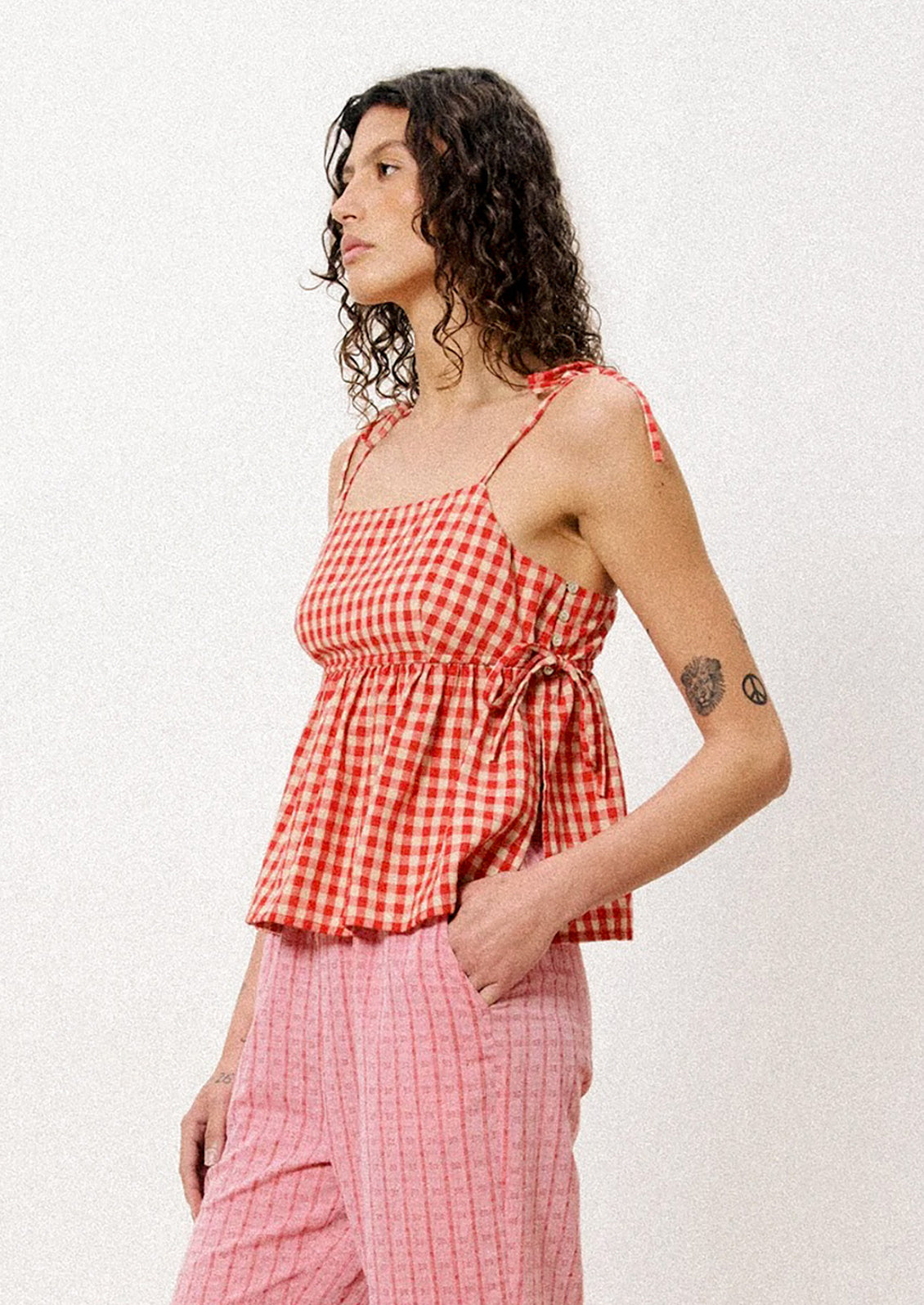 A woman wearing a tank top with shoulder ties in red and beige gingham fabric.