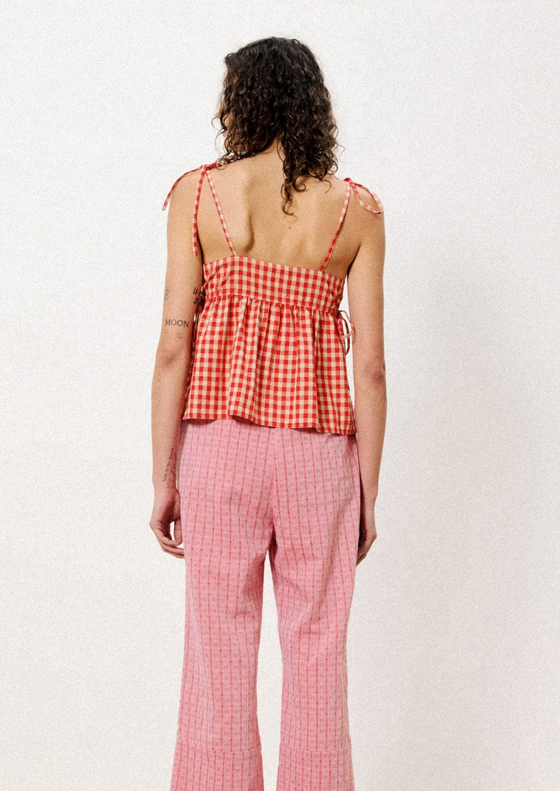 A woman wearing a tank top with shoulder ties in red and beige gingham fabric.