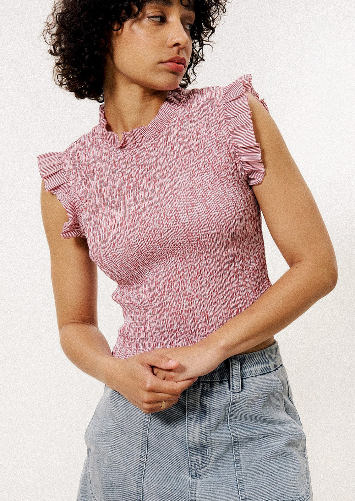 A woman wearing a sleeveless smocked blouse in red and white pinstripe.