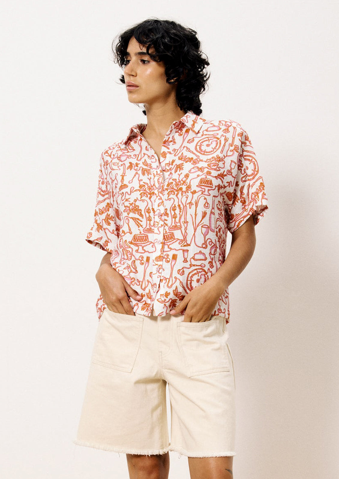 A person wearing a short sleeve button front shirt with pink and orange set the table print.