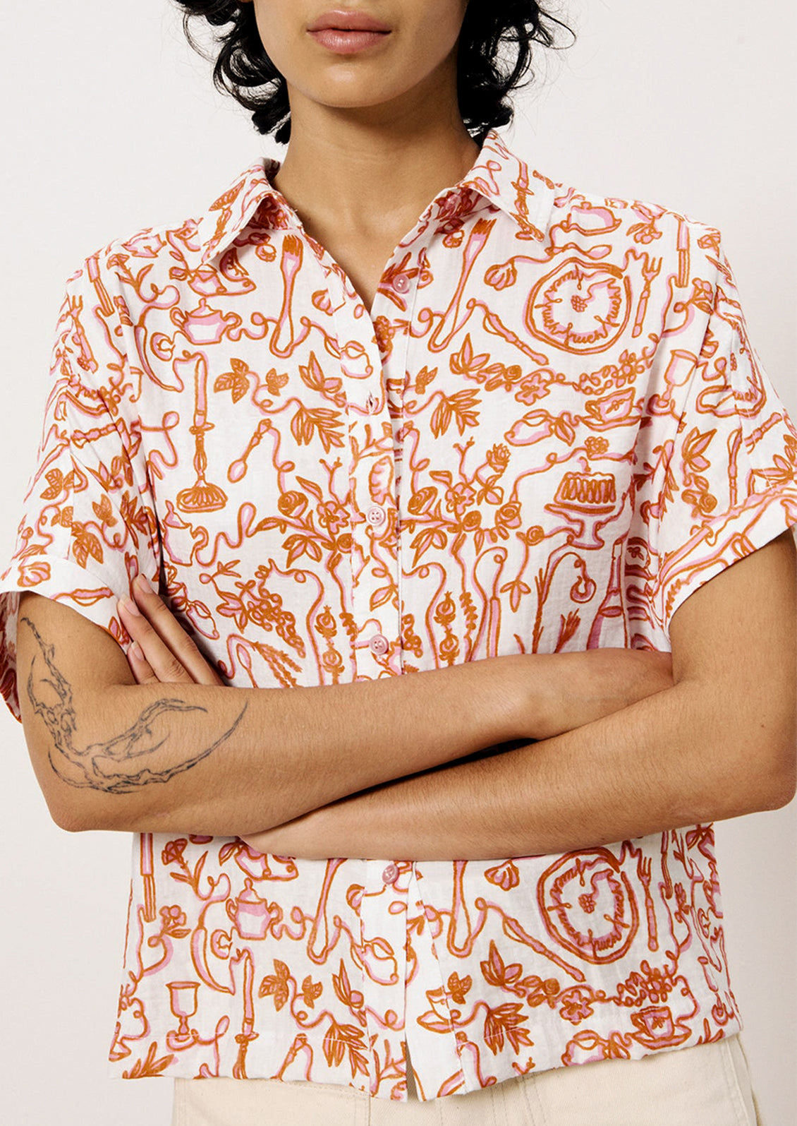 A person wearing a short sleeve button front shirt with pink and orange set the table print.