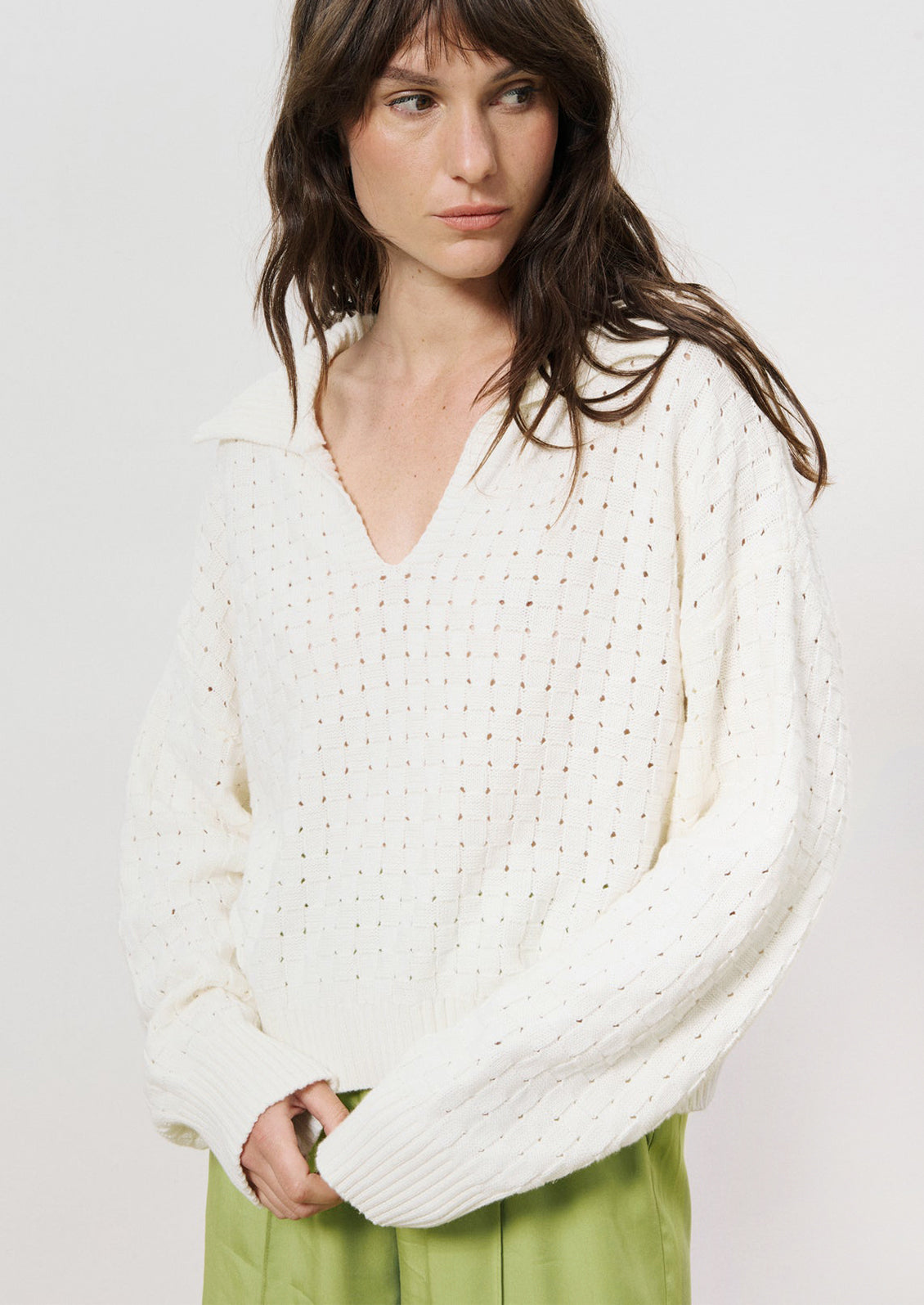 A woman wearing a collared v-neck sweater with woven texture in white.