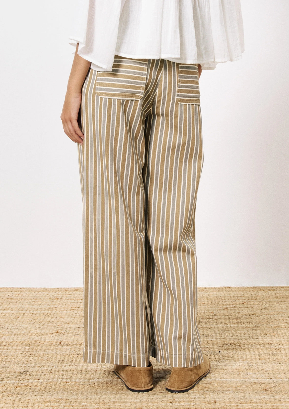 A person wearing a pair of wide leg pants in grey and brown vertical stripe pattern.