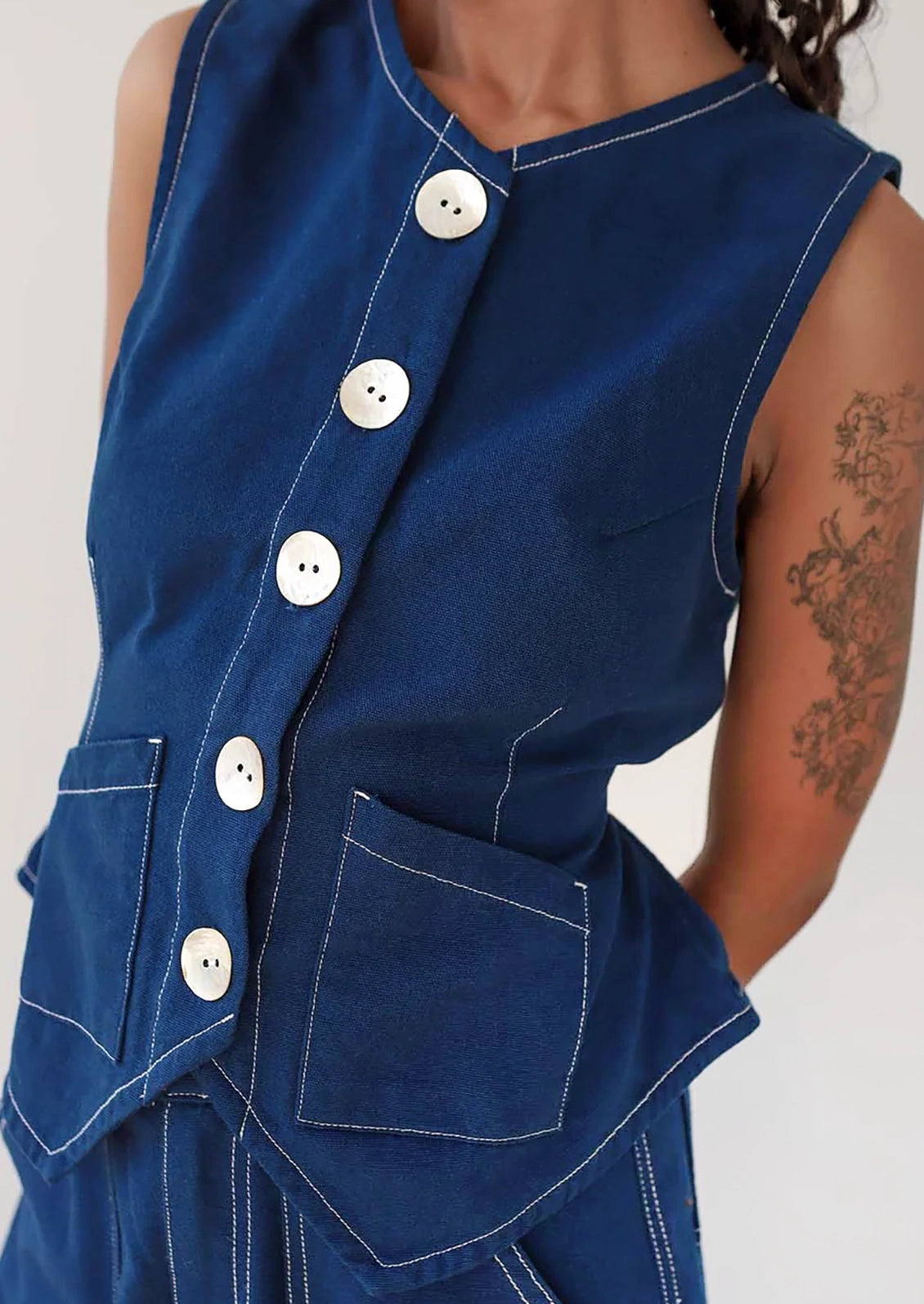 A person wearing a navy sleeveless top with large white shell buttons.