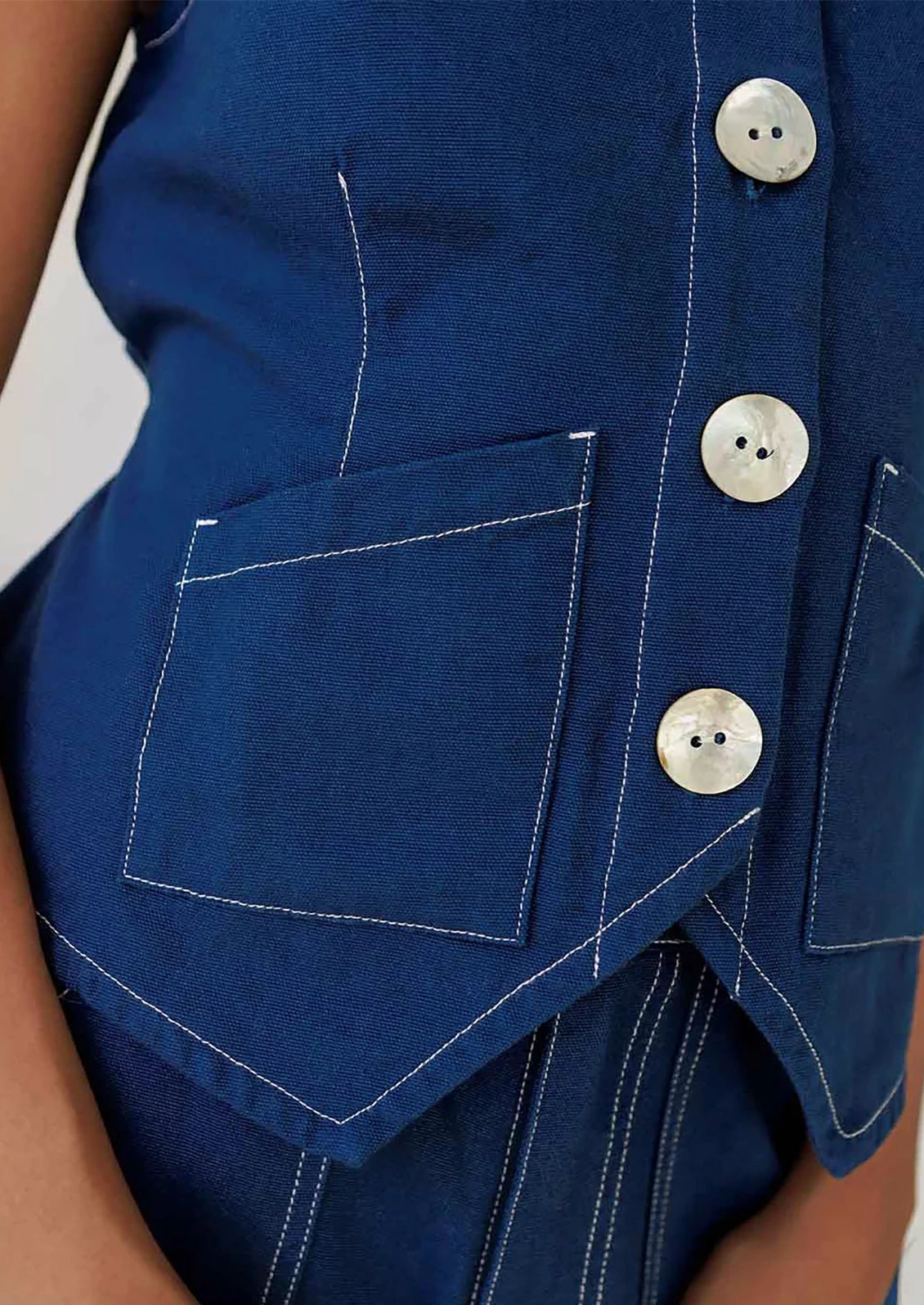 A person wearing a navy sleeveless top with large white shell buttons.