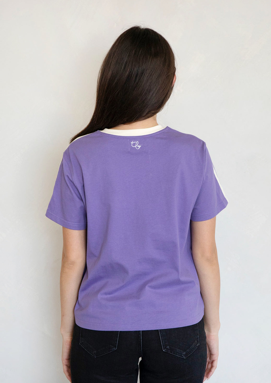 A woman wearing a purple t-shirt with white racing stripes at shoulders.