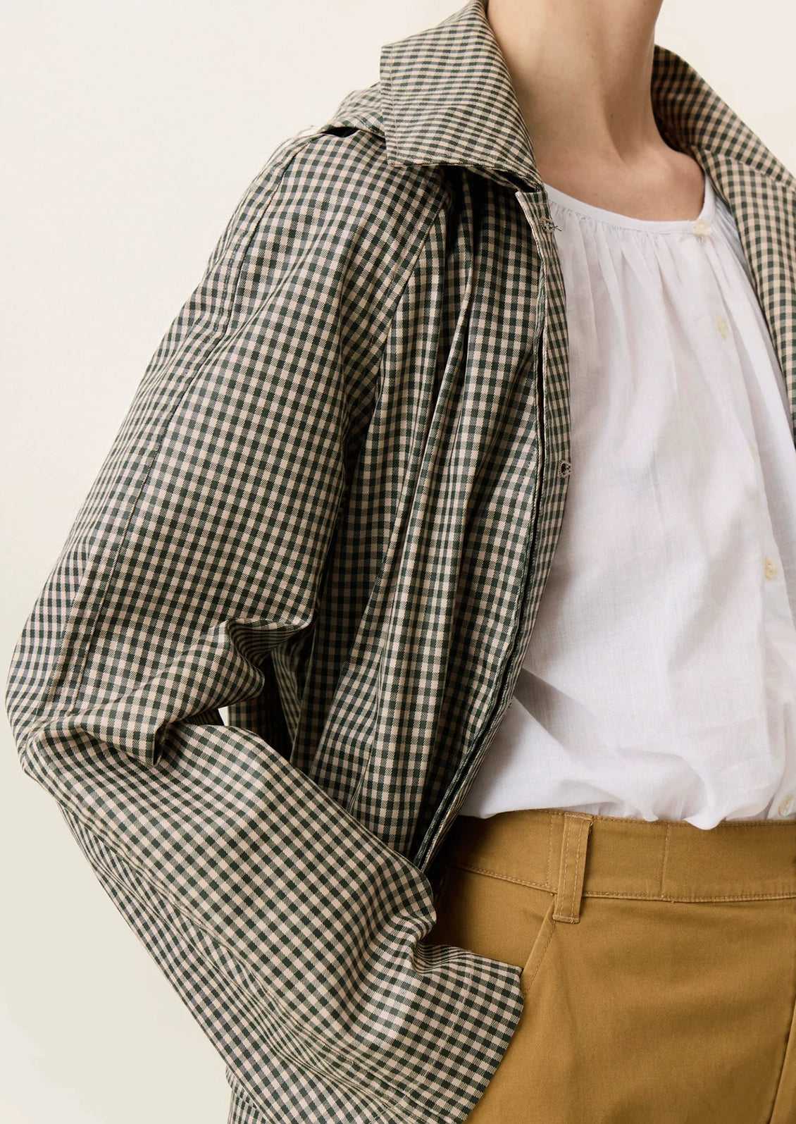 A woman wearing a trench coat in small green and beige gingham pattern.
