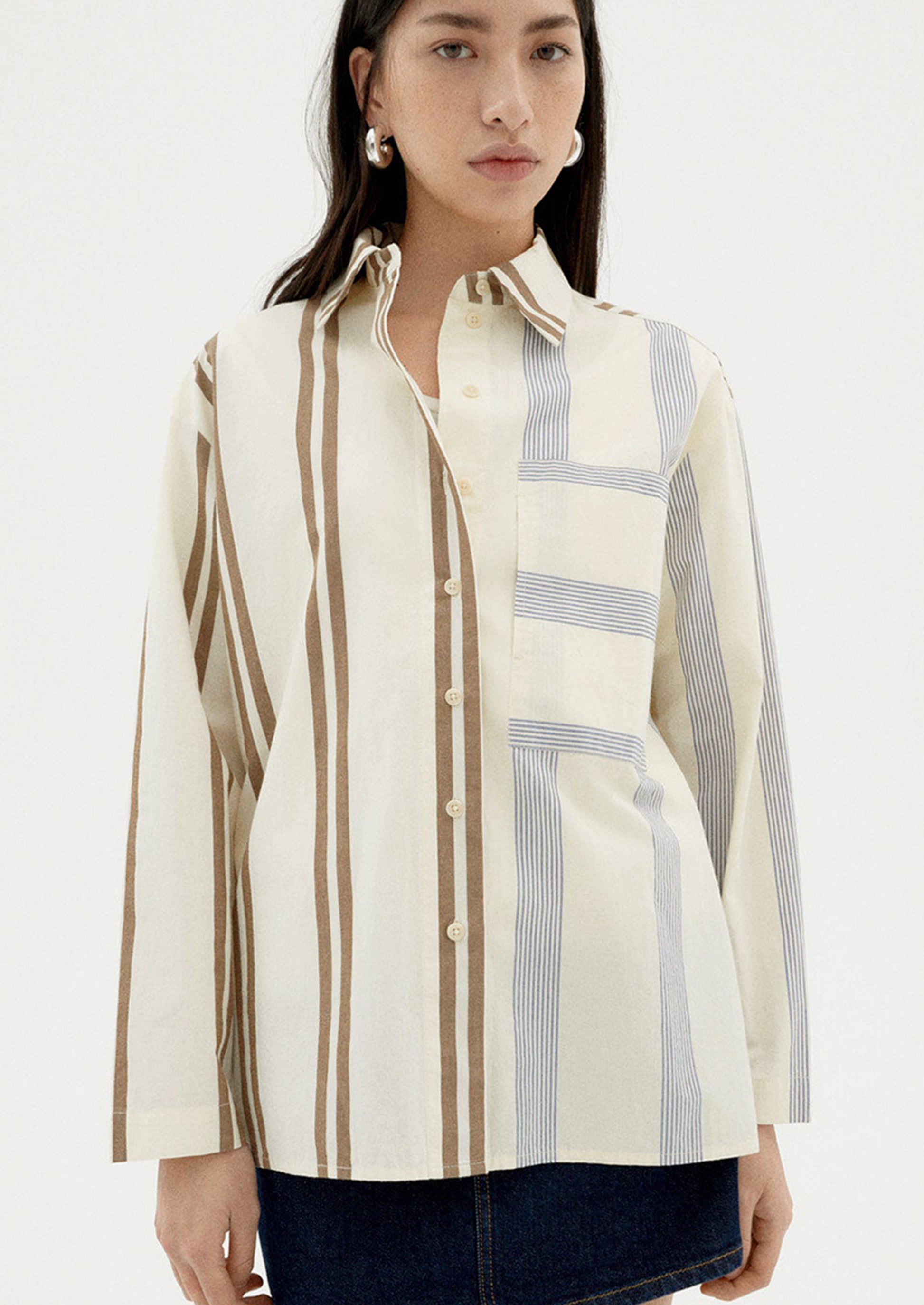 A woman wearing a button down collared shirt with half brown stripes, half blue stripes.
