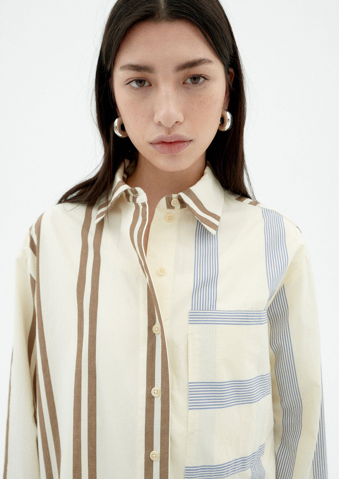 A woman wearing a button down collared shirt with half brown stripes, half blue stripes.