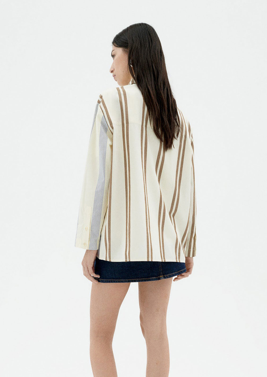 A woman wearing a button down collared shirt with half brown stripes, half blue stripes.