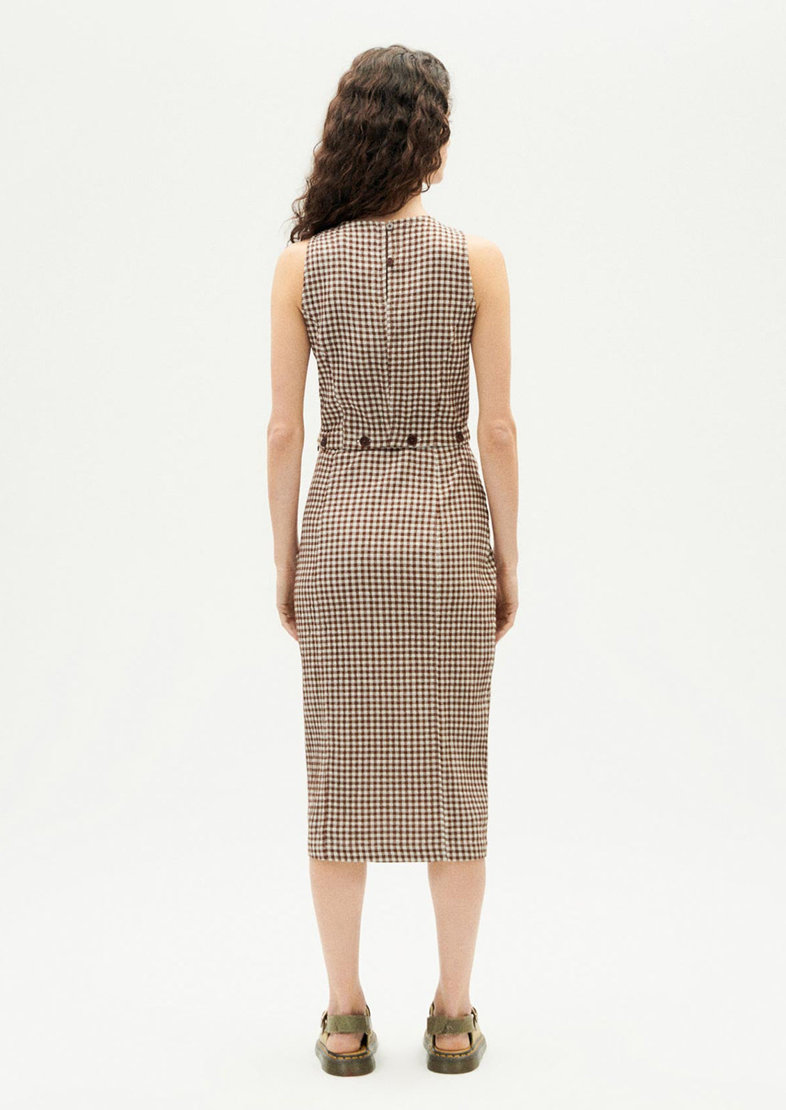 A woman wearing a sleeveless shift dress with button waist detail.