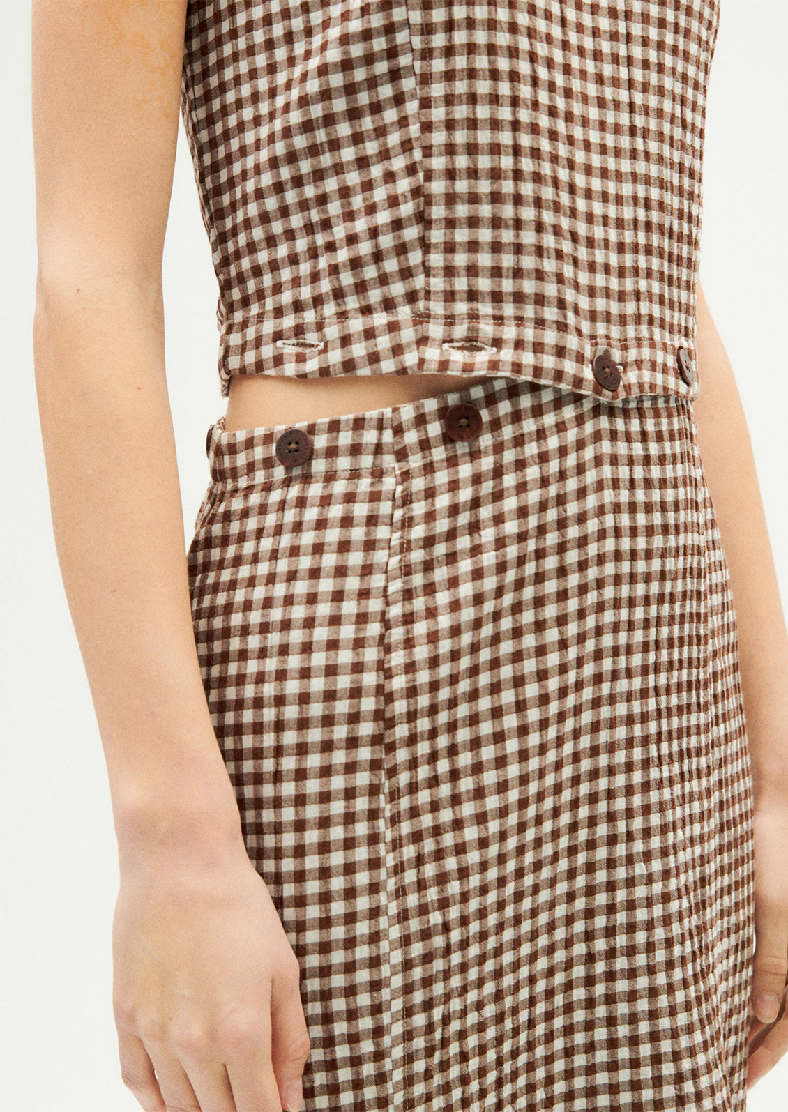 A woman wearing a sleeveless shift dress with button waist detail.