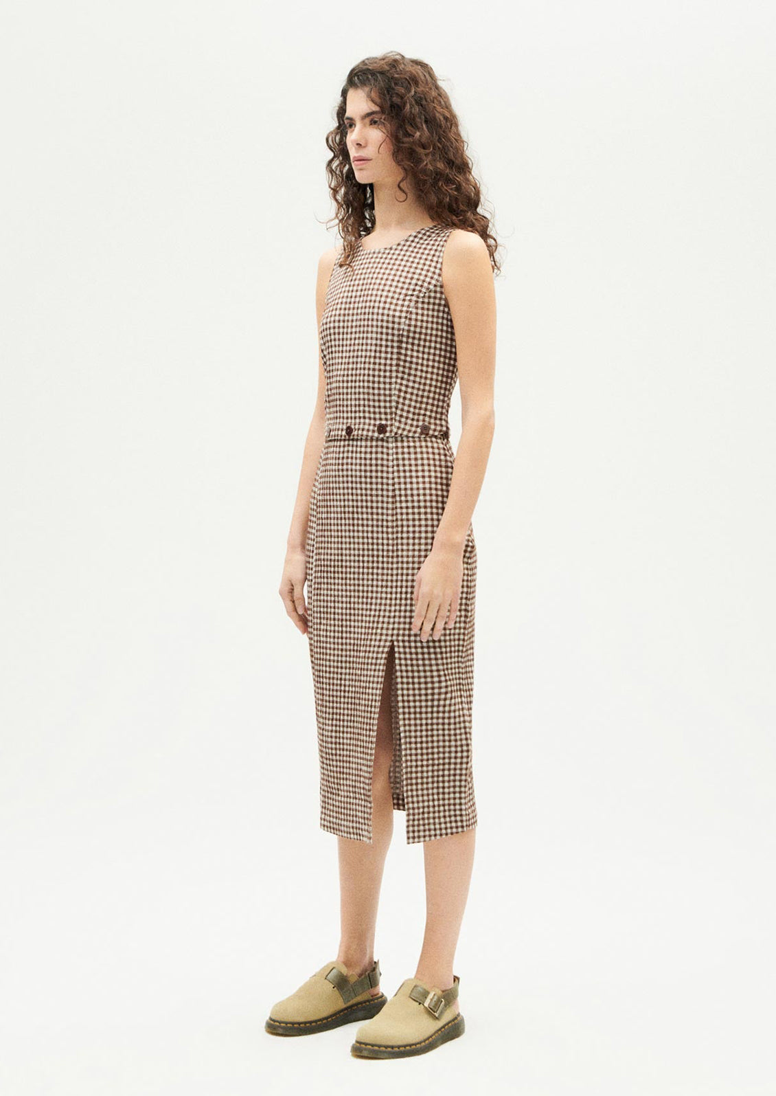 A woman wearing a sleeveless shift dress with button waist detail.