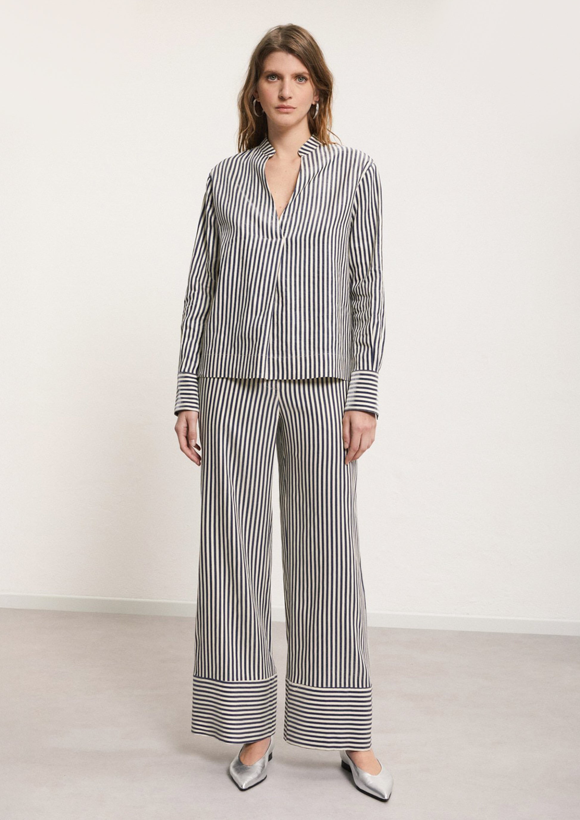 A woman wearing a striped long sleeve shirt in metallic navy blue and cream stripe.