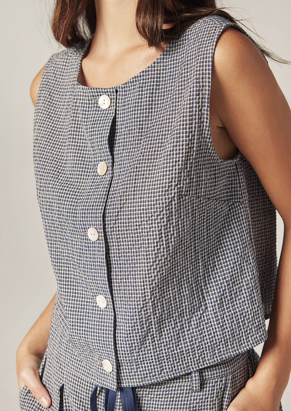A person wearing a sleeveless shell top in navy and white gingham.