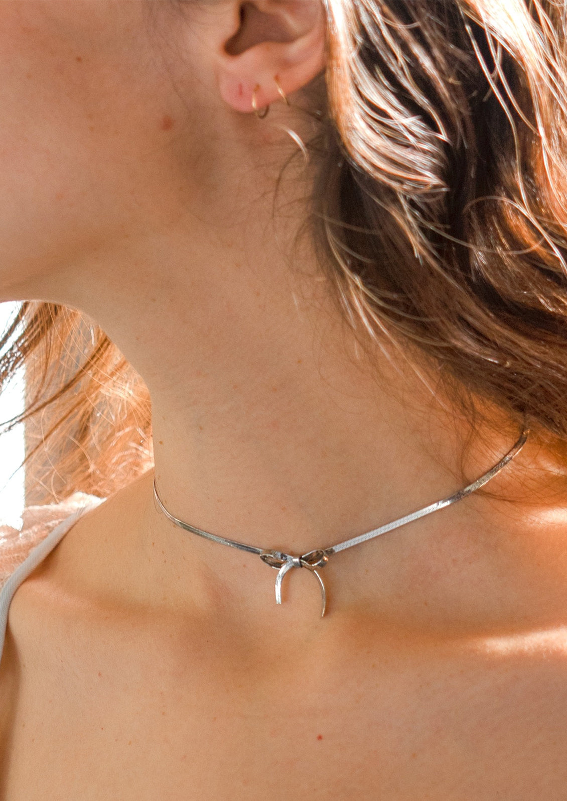 A woman wearing a silver choker-style necklace with bow shape at front.
