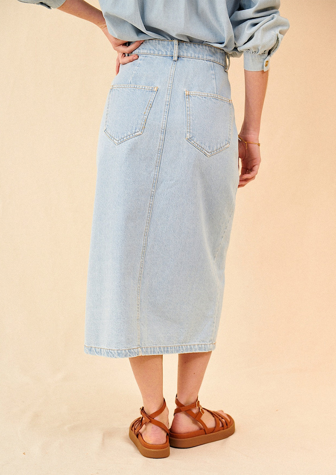 A woman standing wearing a midi length denim skirt featuring back pocket detail
