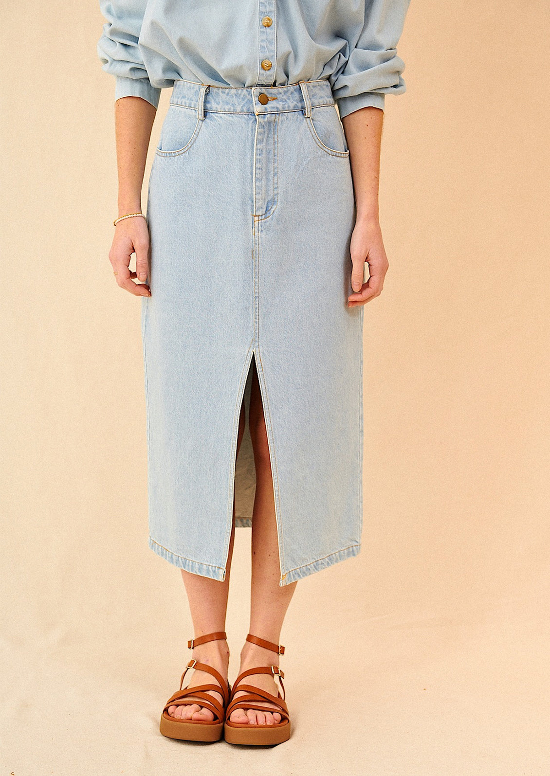 A woman standing wearing a midi length denim skirt with brown sandals