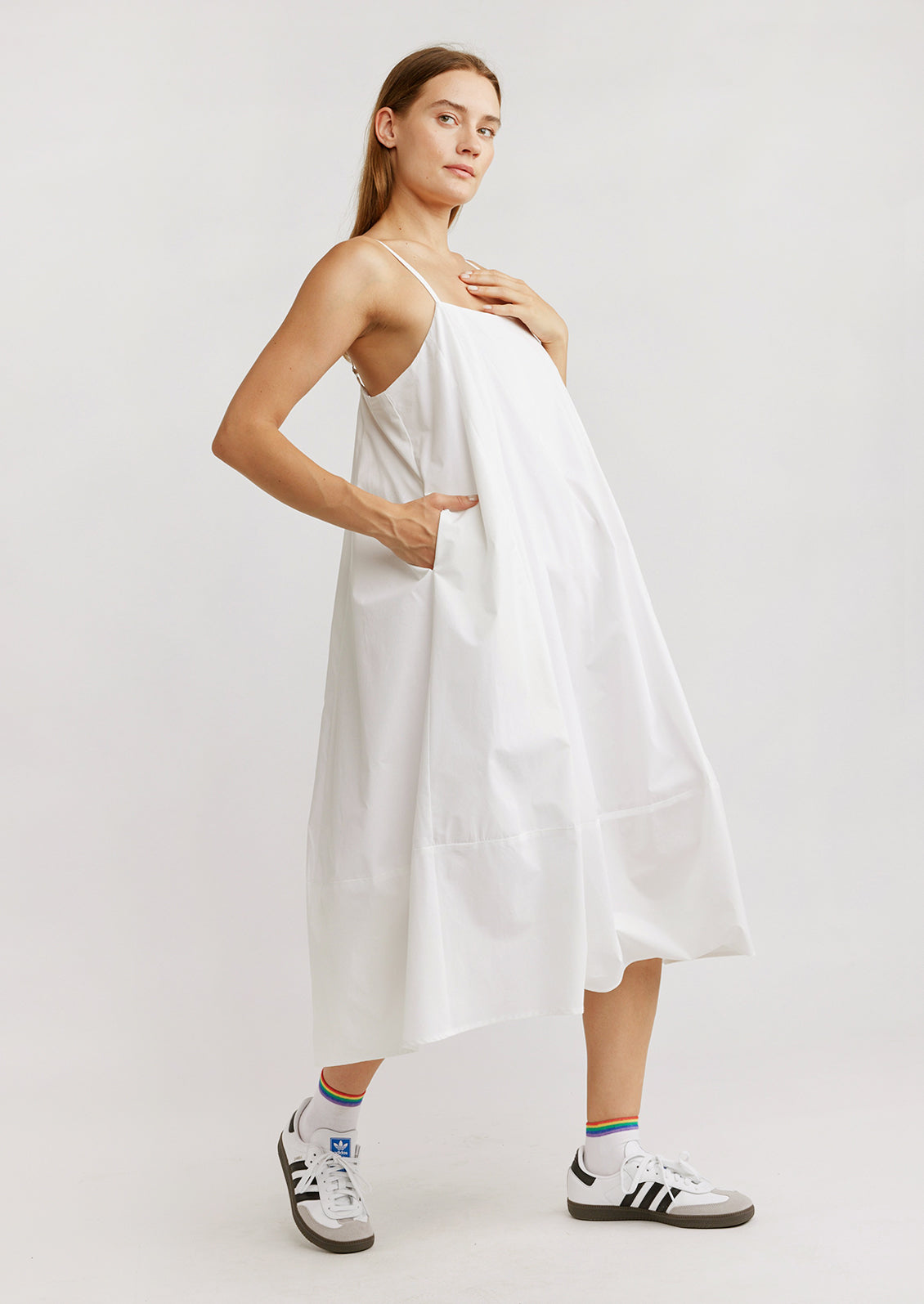 A woman standing wearing a white cotton dress with sneakers