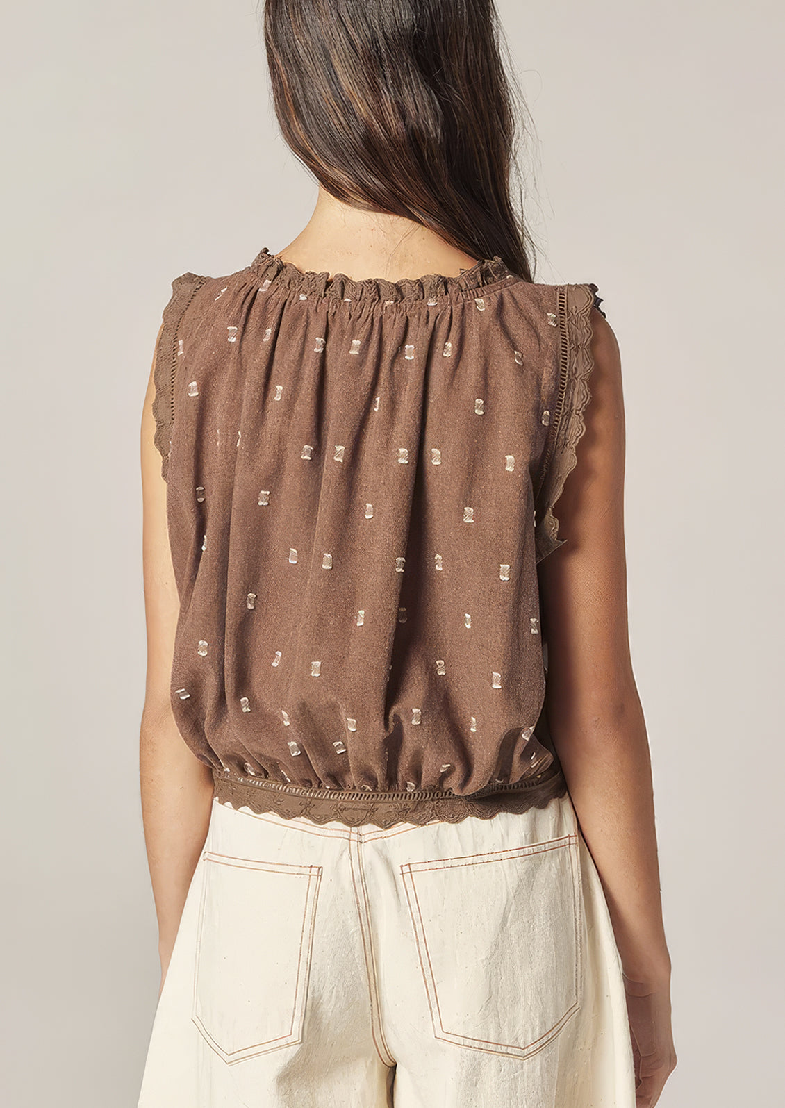 A person wearing a brown sleeveless top with white swiss dot detailing.