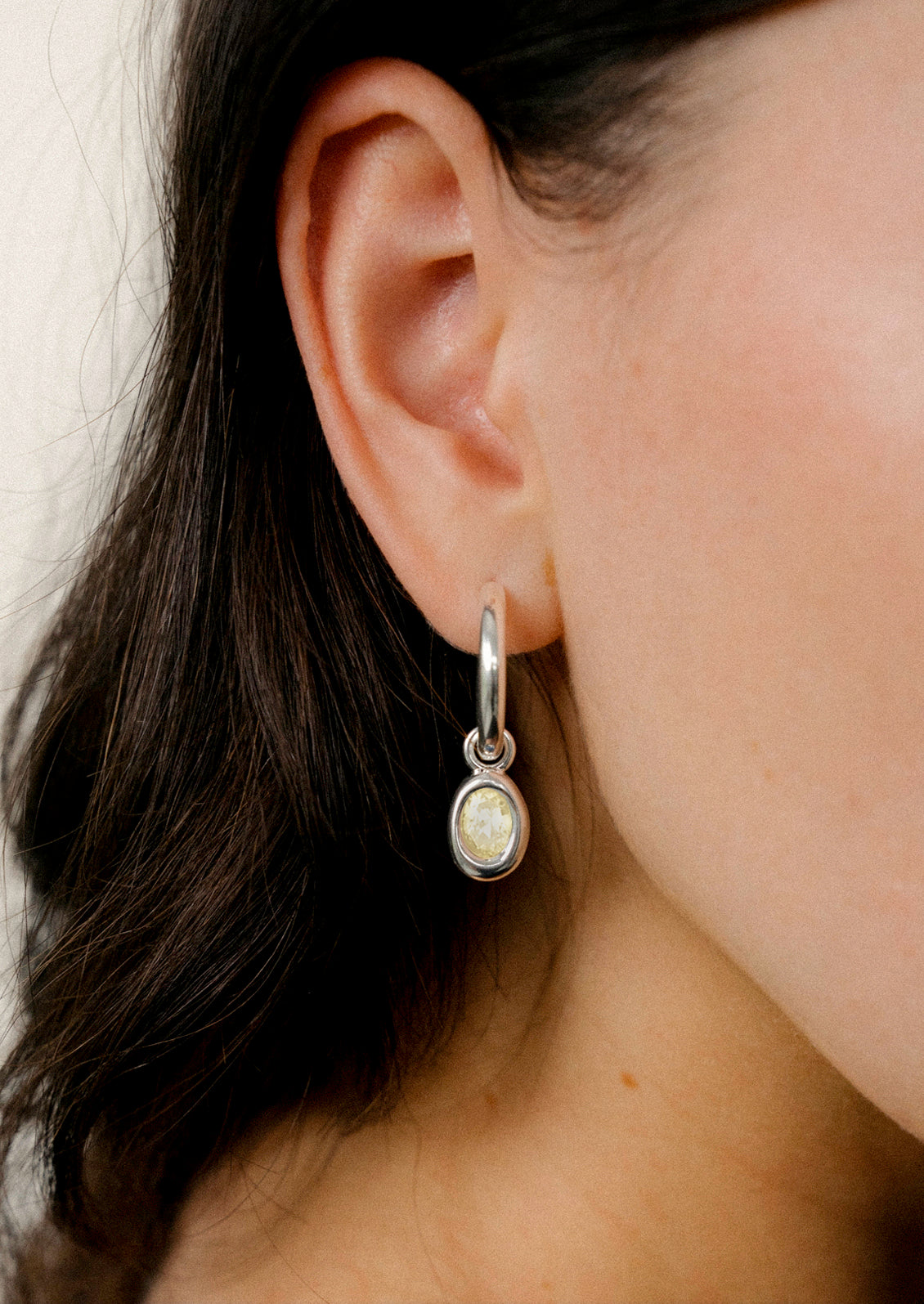 A woman wearing a sterling silver hoop earring with a pale yellow gem.