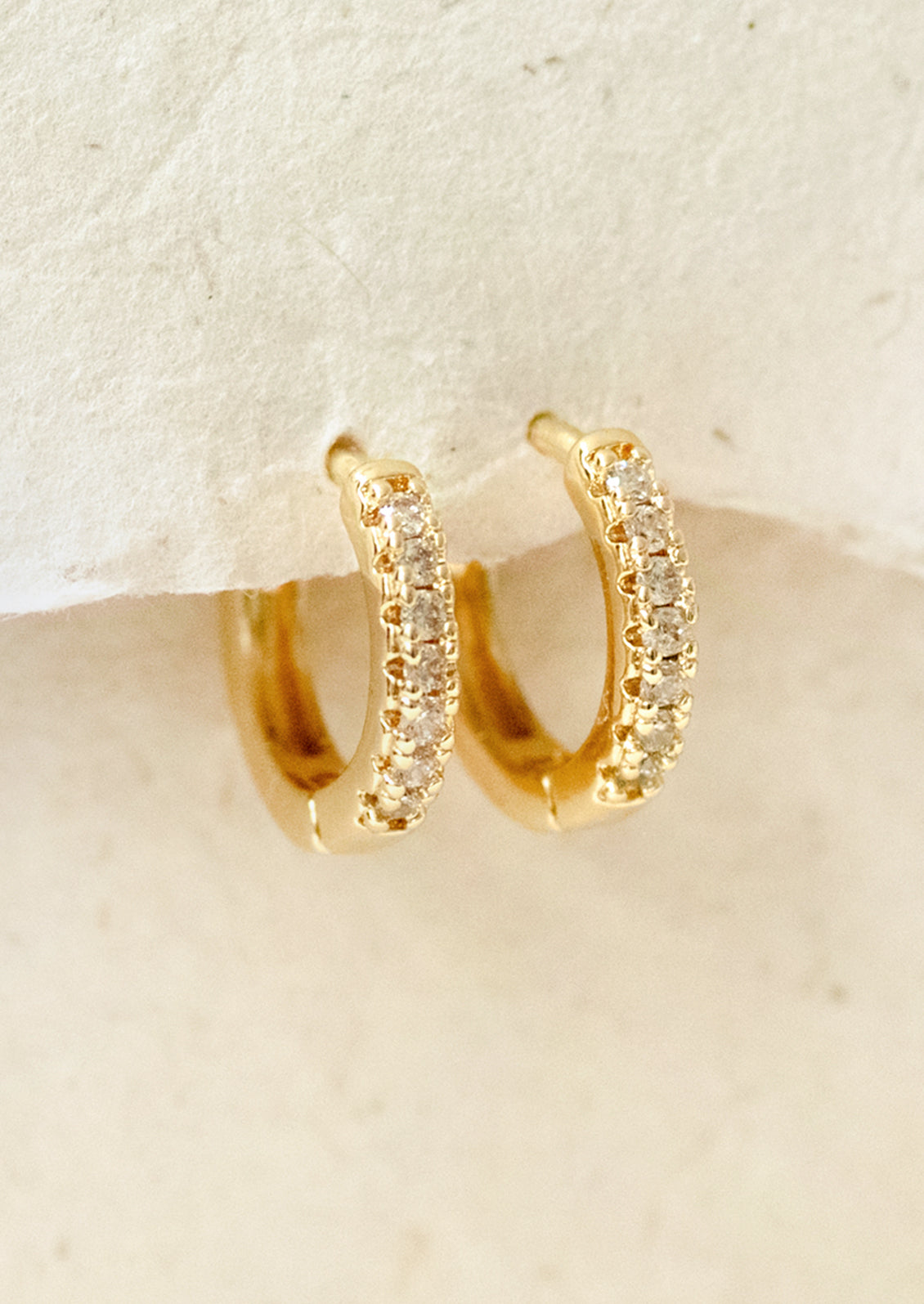 A pair of small huggie hoop earrings with cubic zirconia pave detailing.