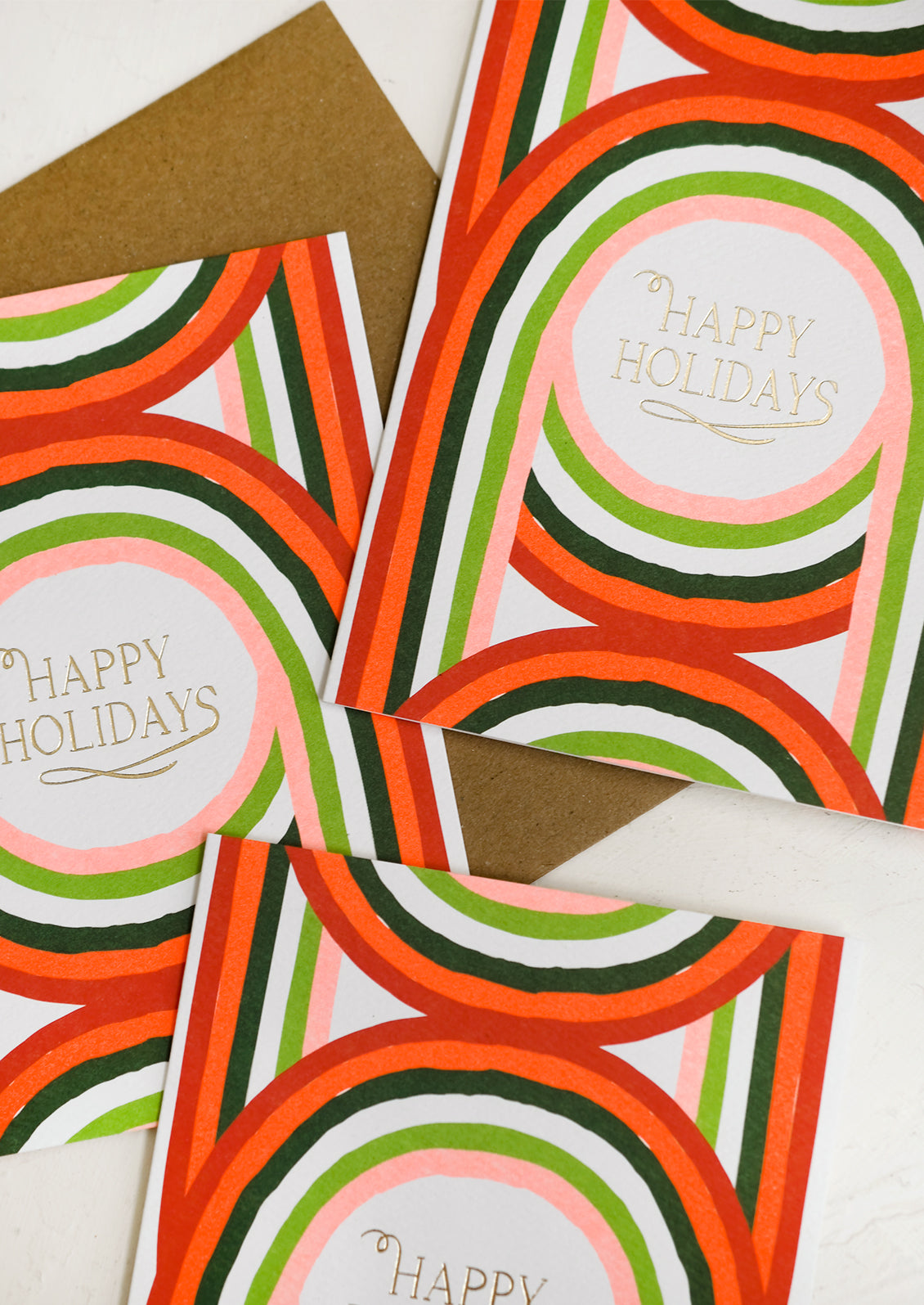A holiday card set with geometric arch print in red and green, text reads "happy holidays".