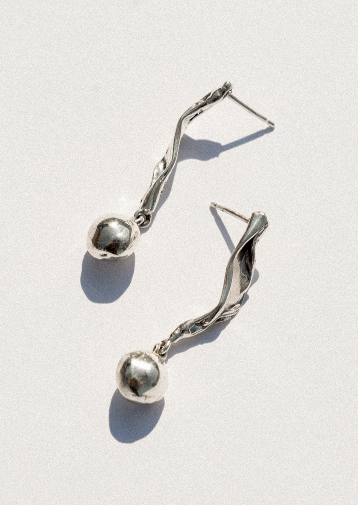 A pair of silver dangle earrings with twisted wire details and small polished spherical beads, photographed on a light gray background with sharp shadows.