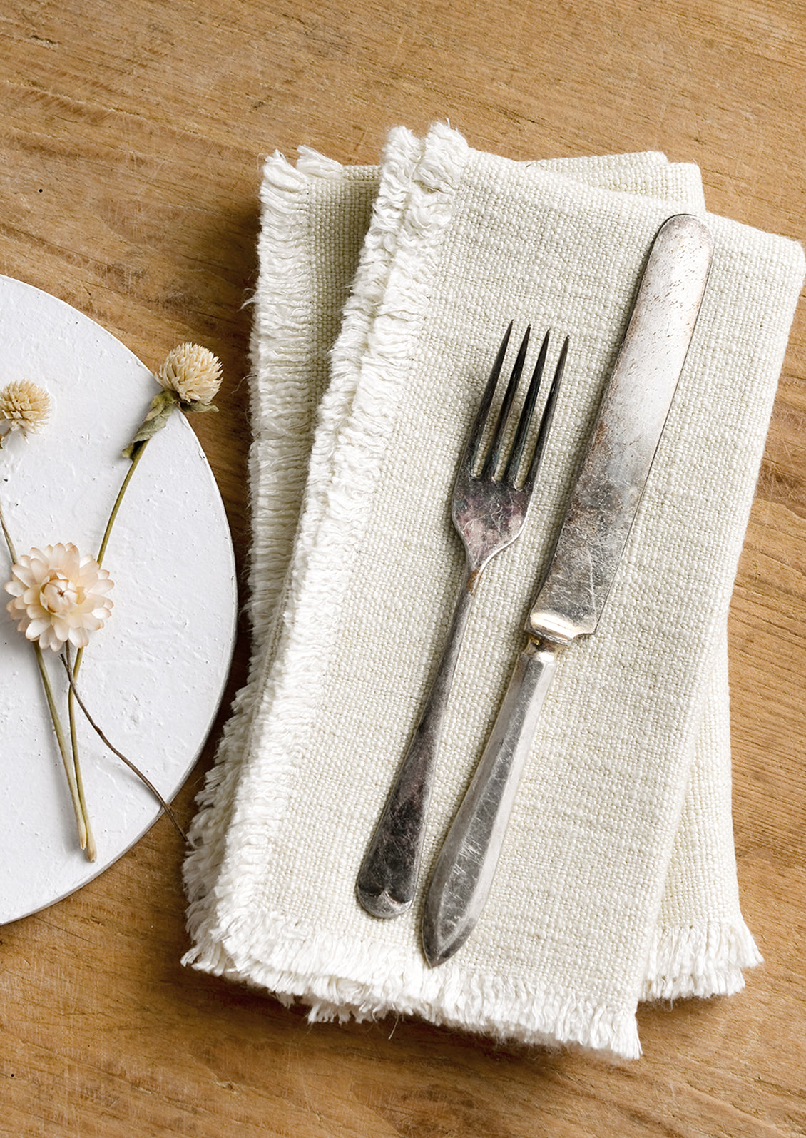 A pair of cream linen napkins with linen texture and fringed edges.
