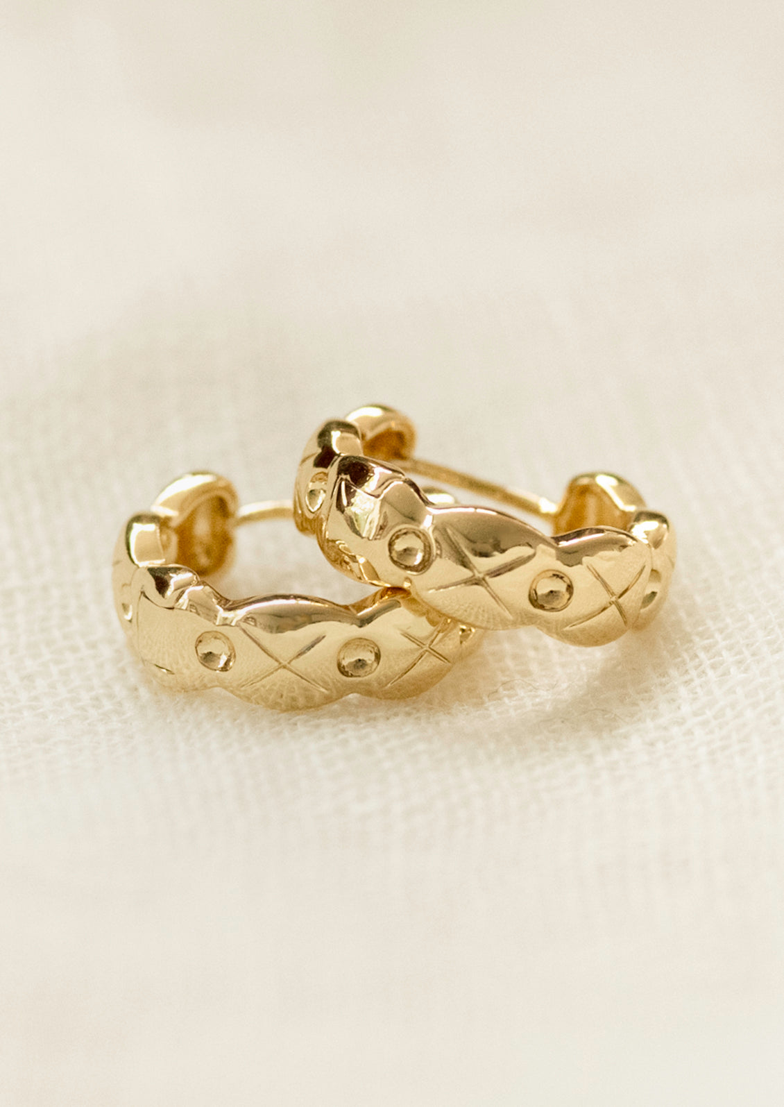 A pair of gold huggie hoop earrings with wavy edges and an etched design.