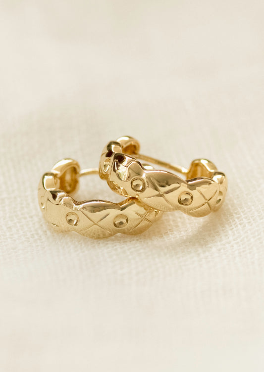 A pair of gold huggie hoop earrings with wavy edges and an etched design.