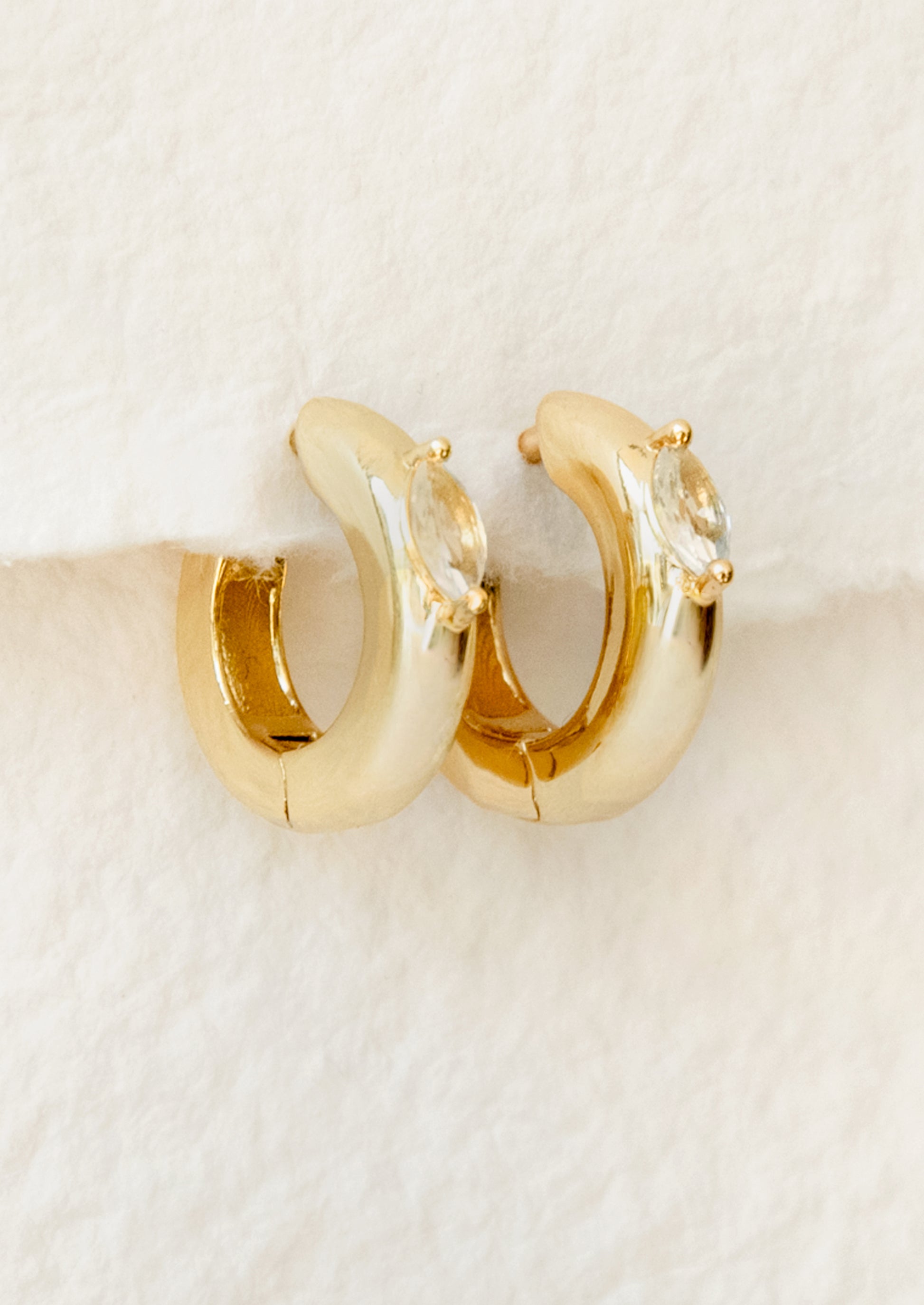 Gold hoop earrings with clear gemstones on a beige background