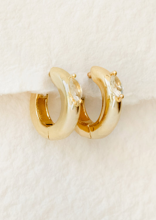 Gold hoop earrings with clear gemstones on a beige background