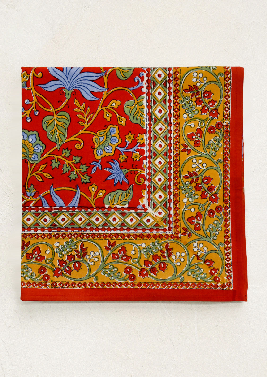 A block printed tablecloth in red with mustard, blue and green floral print.