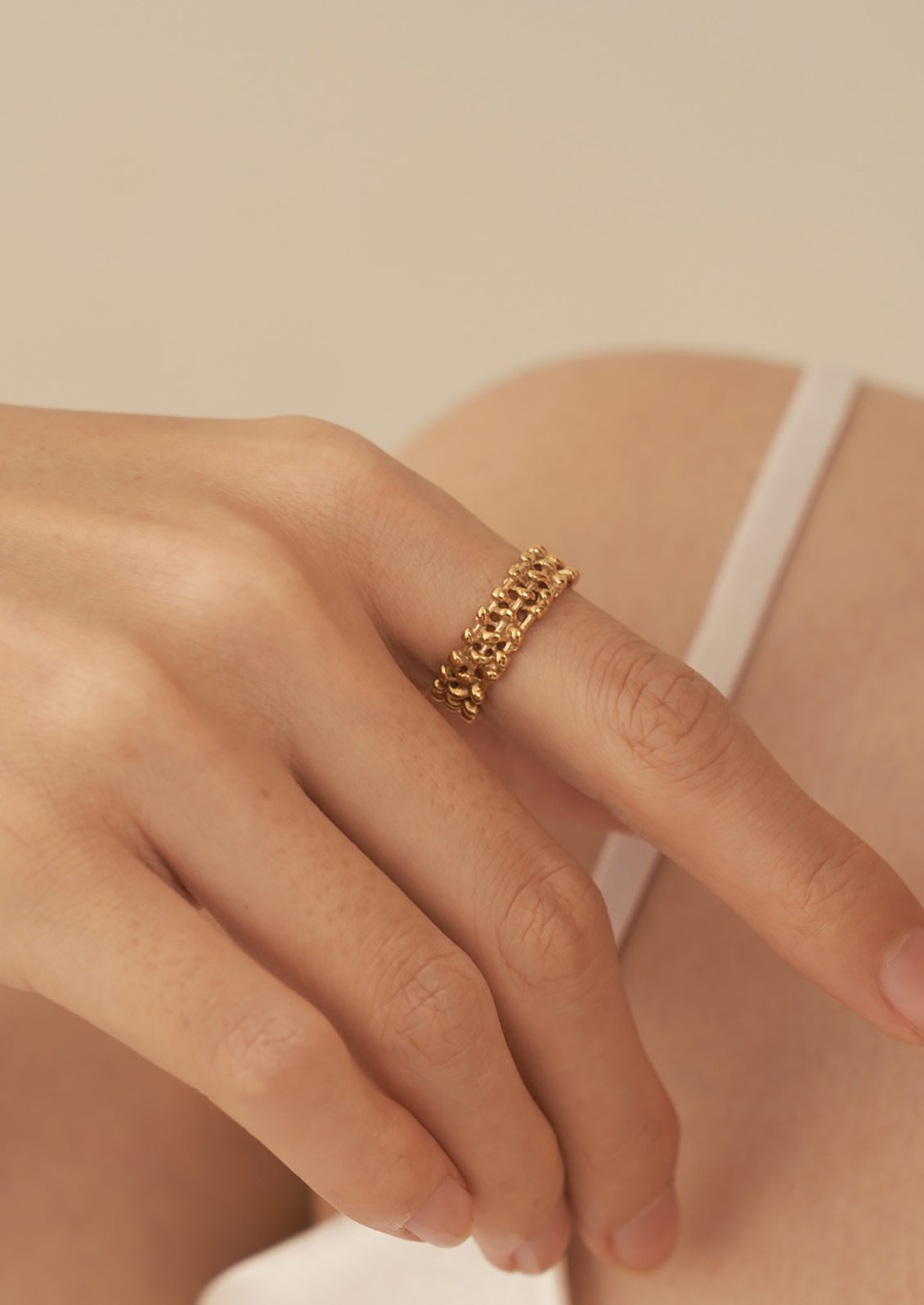 A person wearing a gold ring with thick woven textured band.