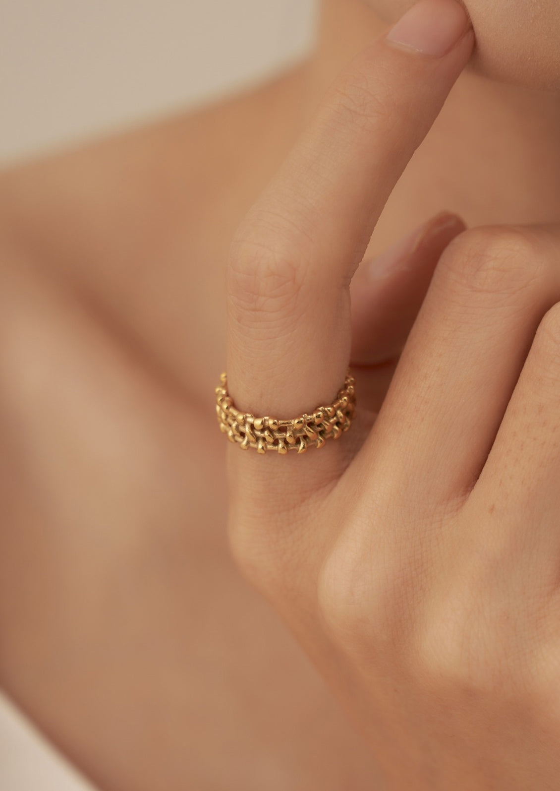 A person wearing a gold ring with thick woven textured band.