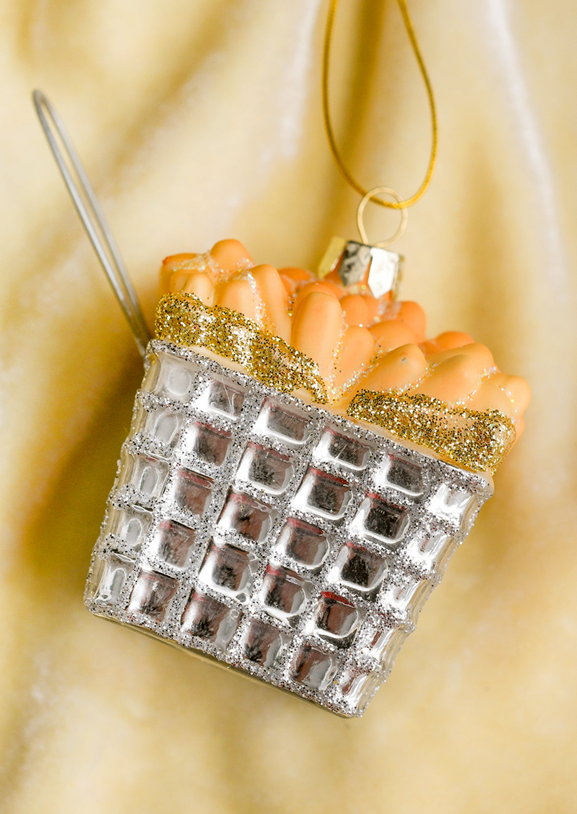 A glass ornament of french fries in a silver frying basket with handle.