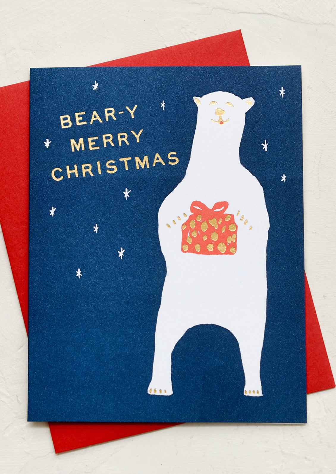 A greeting card with illustration of a polar bear holding present, text reads "Bear-y Merry Christmas".