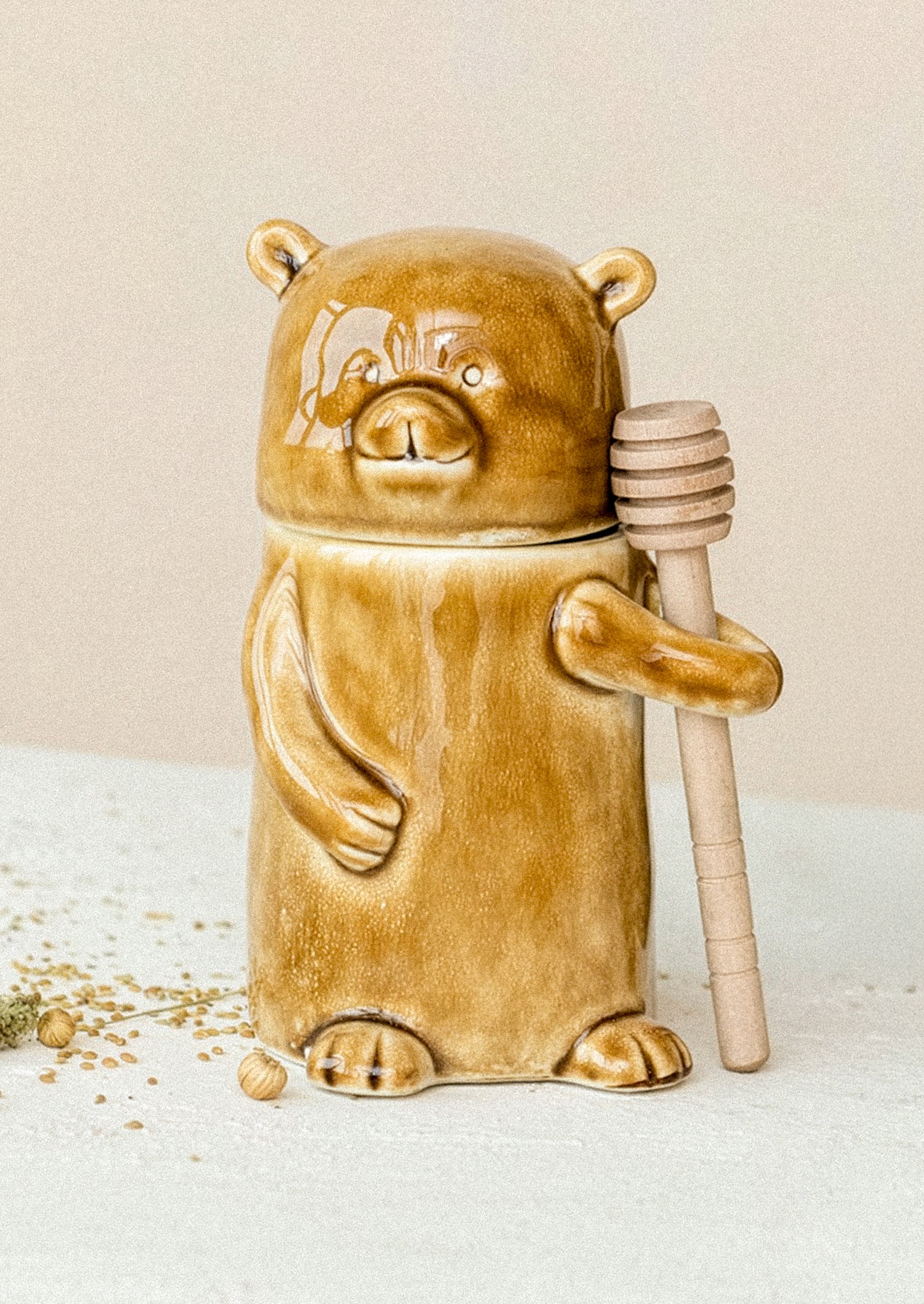 Ceramic honey bear container with a honey dipper on a light surface.