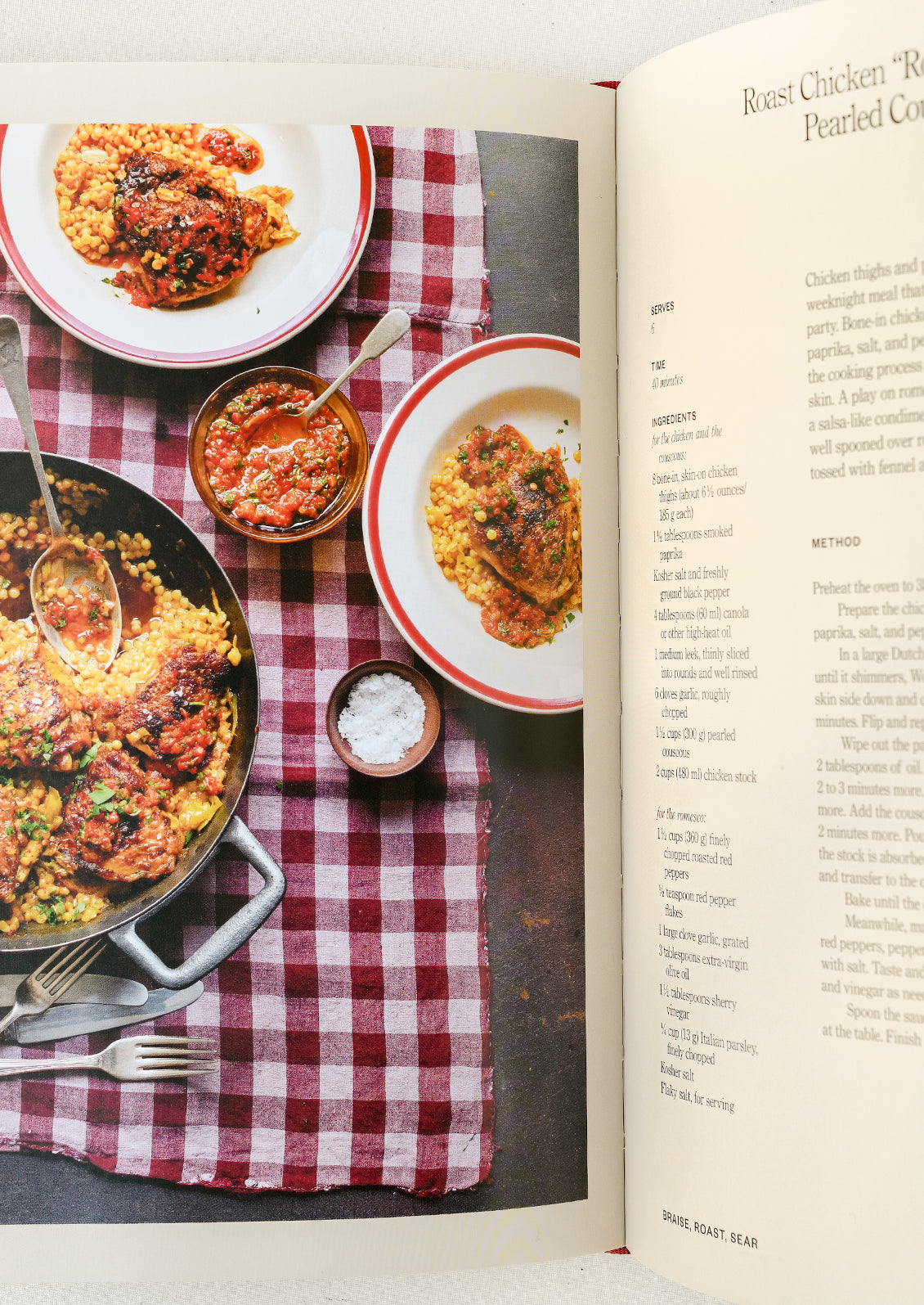A cookbook open on a table with a picture of roasted chicken and couscous.