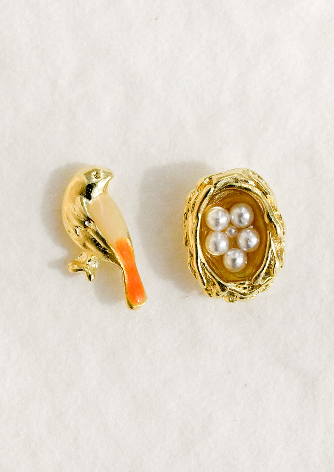 A pair of mismatched gold stud earrings in form of bird and nest.