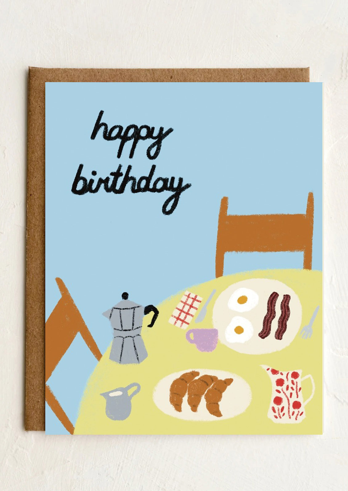 A greeting card with illustration of a breakfast scene on table, text reads "Happy Birthday".