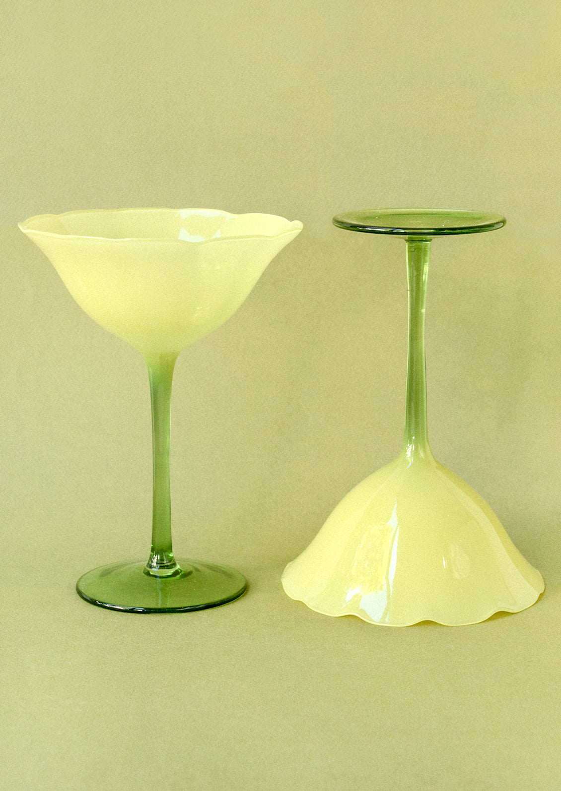 Two coupe glasses in the shape of a flower with a yellow top and green bottom.